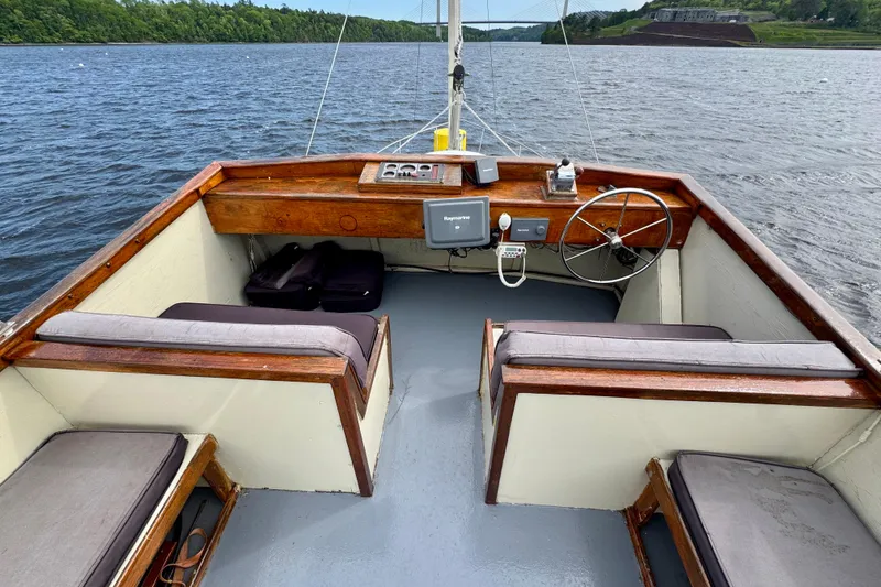 Slide: The Image of 1976 Downeast Flybridge Cruiser with wooden helm, cushioned seating, and scenic water view. - 70