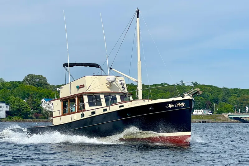Slide: The Image of 1976 Downeast Flybridge Cruiser sailing on a scenic river with lush green shoreline. - 77