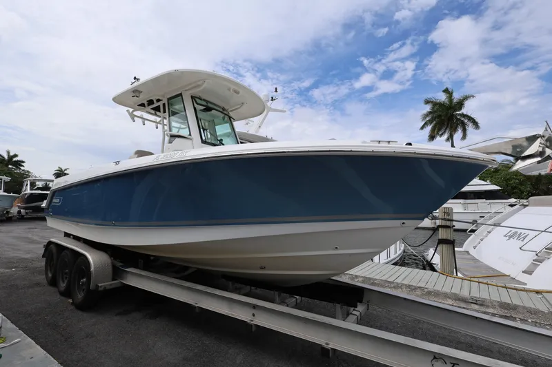 Slide: The Image of 2016 Boston Whaler 250 Outrage boat on trailer, dockside with palm trees and blue sky. - 2