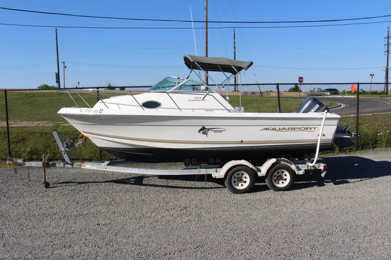 The Image of 2003 Aquasport 215 Explorer boat on trailer, parked outdoors on gravel. - 1