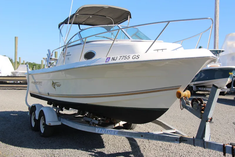 Slide: The Image of 2003 Aquasport 215 Explorer boat on trailer, parked outdoors under clear blue sky. - 11