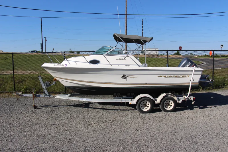 Slide: The Image of 2003 Aquasport 215 Explorer boat on trailer, parked outdoors under clear blue sky. - 2