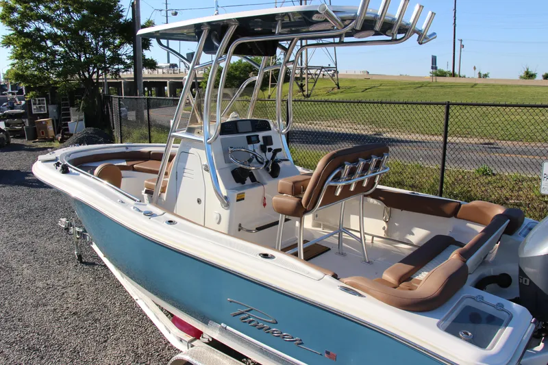 Slide: The Image of 2022 Pioneer 222 Islander boat with blue hull, brown seating, and T-top, parked outdoors. - 5