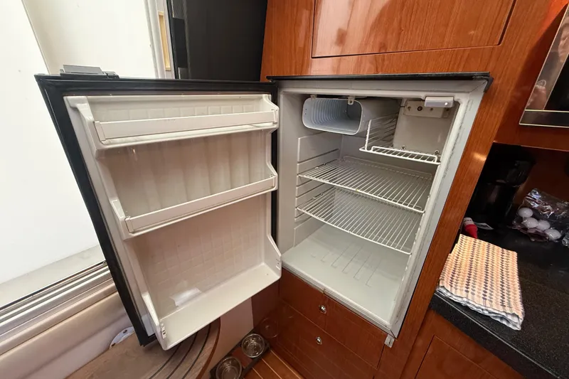 Slide: The Image of Open refrigerator inside 2005 Regal Commodore 3560 IO yacht, featuring wooden cabinetry. - 52