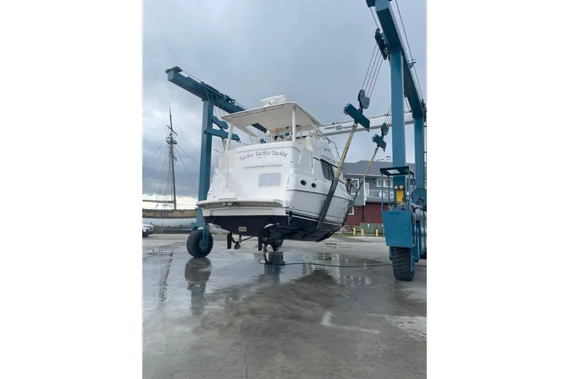 Slide: The Image of 1999 Silverton 322 Motor Yacht being lifted by a boat hoist on a cloudy day. - 27