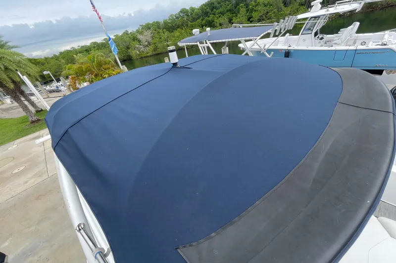 Slide: The Image of 2022 Four Winns HD8 OB boat with blue cover docked near lush greenery. - 44