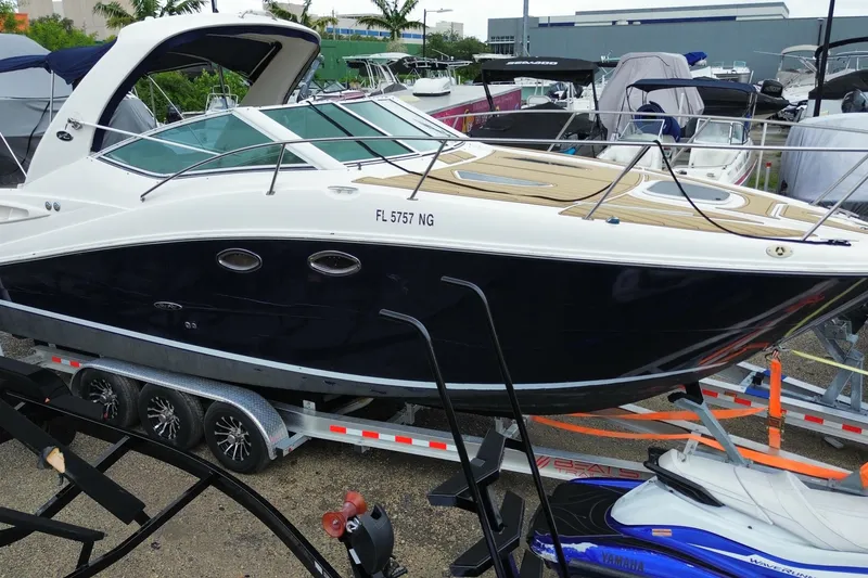 The Image of 2006 Sea Ray 290 Sundancer boat on trailer, parked in marina with other vessels. - 1