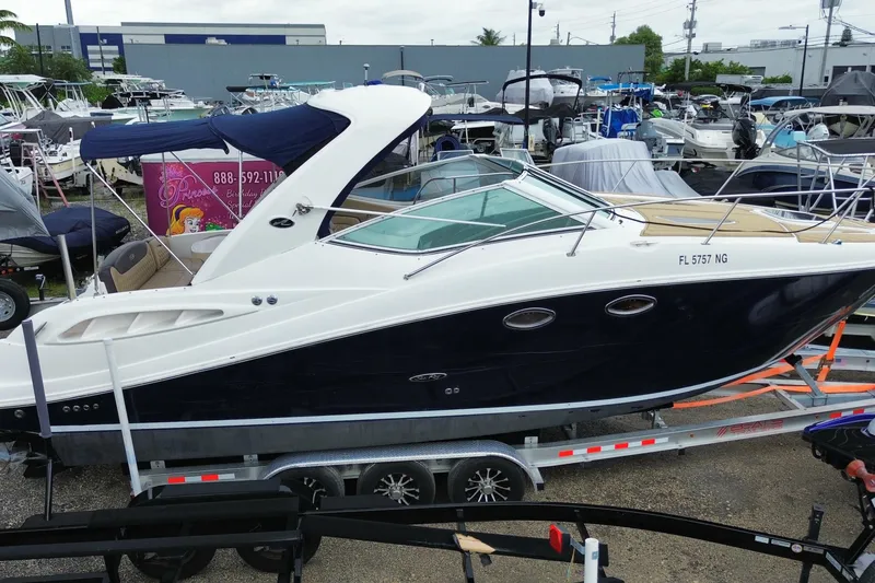 Slide: The Image of 2006 Sea Ray 290 Sundancer boat on trailer in marina, surrounded by other boats. - 13