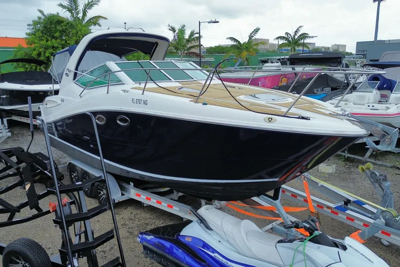 Slide: The Image of 2006 Sea Ray 290 Sundancer boat on trailer, parked outdoors with palm trees in background. - 14