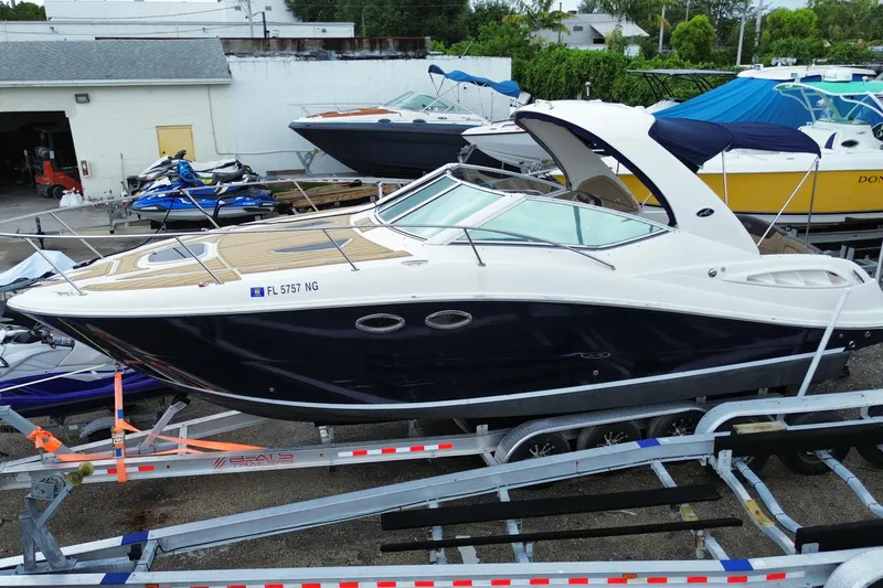 Slide: The Image of 2006 Sea Ray 290 Sundancer boat on trailer, parked in marina with other vessels. - 2