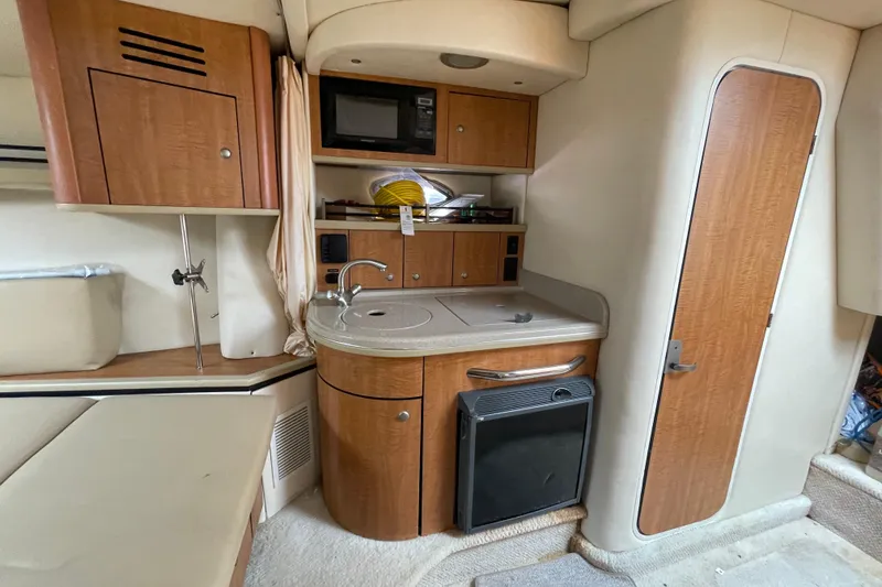 Slide: The Image of 2006 Sea Ray 290 Sundancer cabin with kitchenette, featuring wood cabinetry and compact appliances. - 43