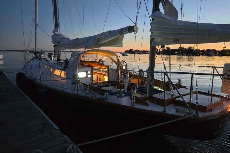 Slide: The Image of 1970 Hinckley Bermuda 40 sailboat docked at sunset, interior lights glowing warmly. - 149