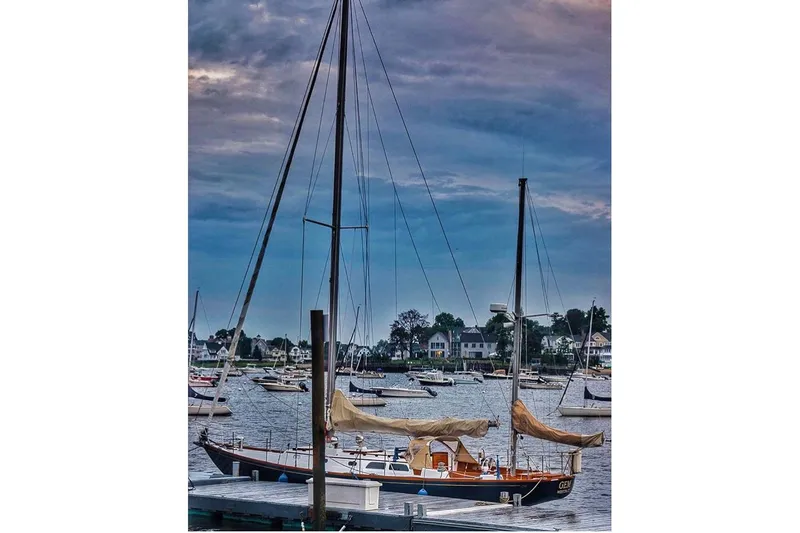 Slide: The Image of 1970 Hinckley Bermuda 40 sailboat docked in a scenic harbor under a cloudy sky. - 6