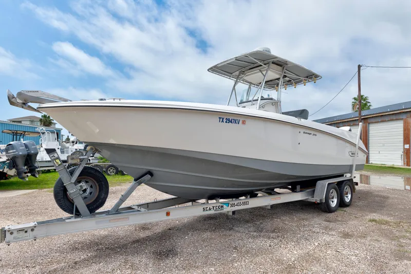 The Image of 2003 Boston Whaler 270 Outrage boat on trailer, parked outdoors under cloudy sky. - 0