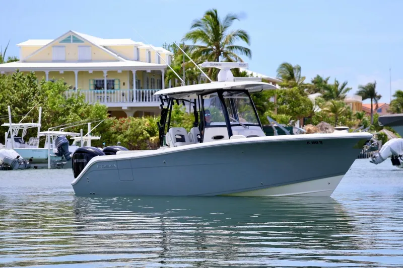 The Image of 2022 Cobia 301 Center Console boat on calm water near a tropical house. - 1