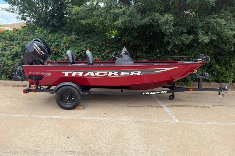 Slide: The Image of 2026 Tracker Super Guide V-16 SC boat, red, parked on pavement with greenery background. - 15