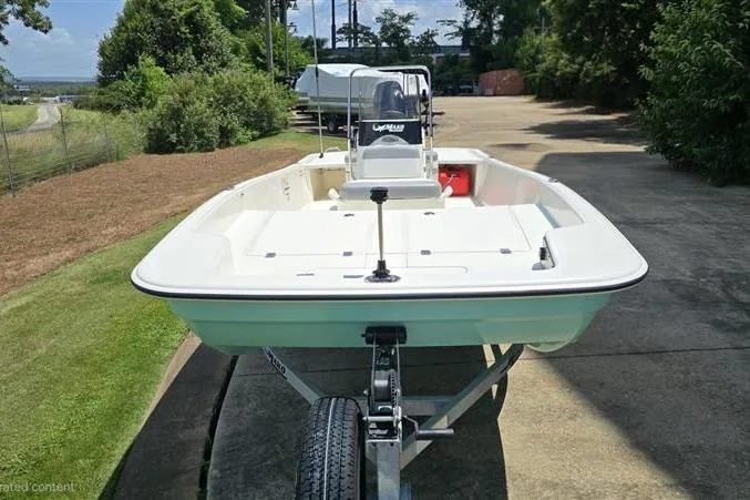 Slide: The Image of 2026 Mako Pro Skiff 17 CC boat on trailer, parked outdoors, surrounded by greenery. - 2
