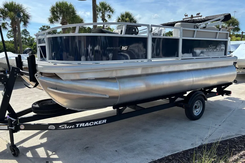 Slide: The Image of 2026 Sun Tracker Bass Buggy 16 XL Select pontoon boat on trailer, parked outdoors. - 73