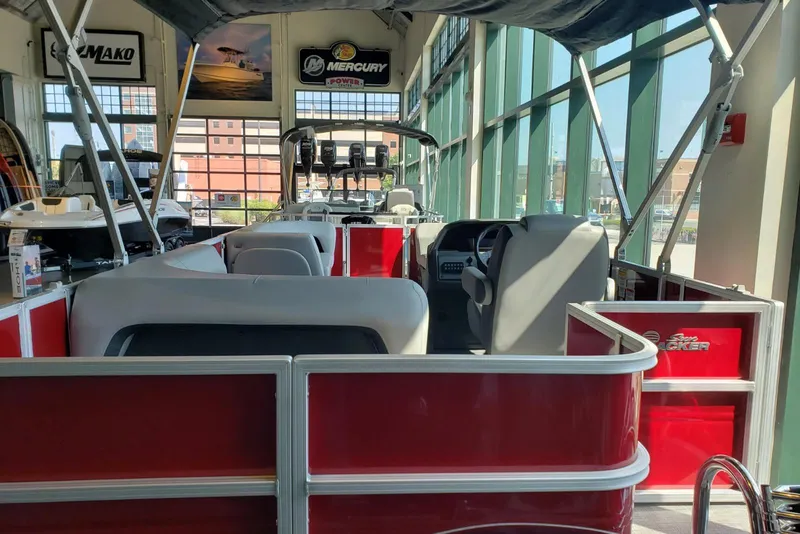 Slide: The Image of 2026 Sun Tracker Party Barge 18 DLX pontoon boat interior in showroom, featuring red and gray seating. - 1