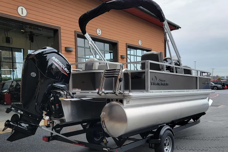 Slide: The Image of 2026 Sun Tracker Bass Buggy 18 DLX pontoon boat with Mercury engine, parked outside. - 3