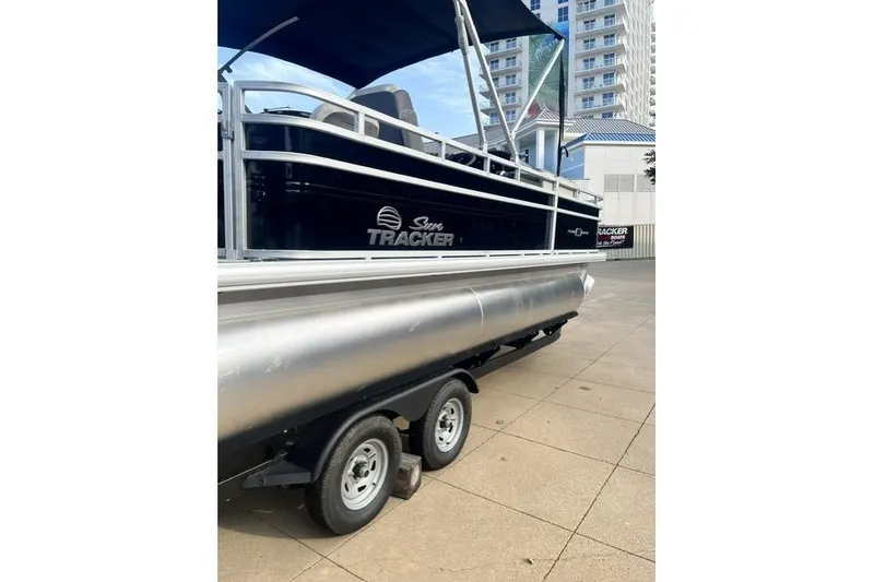 Slide: The Image of 2026 Sun Tracker Fishin' Barge 20 DLX pontoon boat on trailer, urban background. - 2