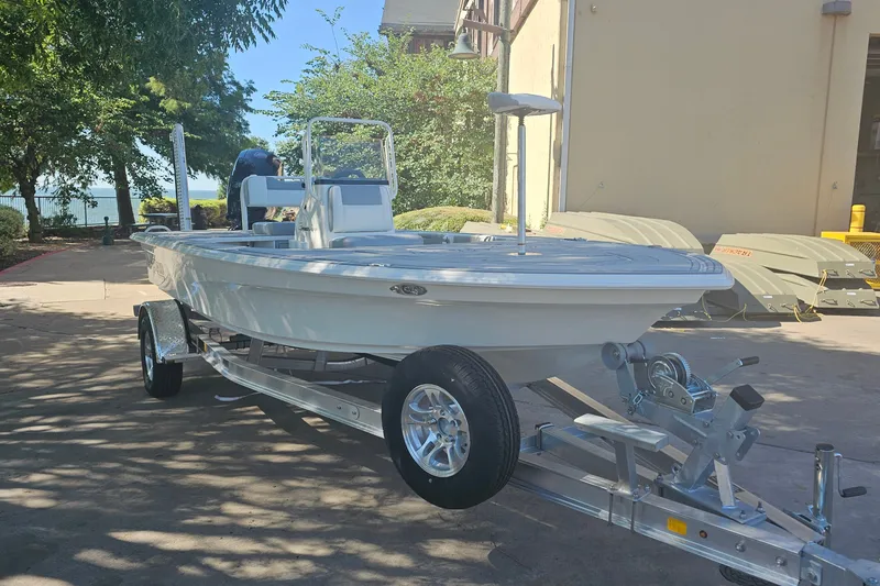 Slide: The Image of 2026 Mako 18 Pro Skiff boat on trailer, parked outdoors near trees and building. - 2