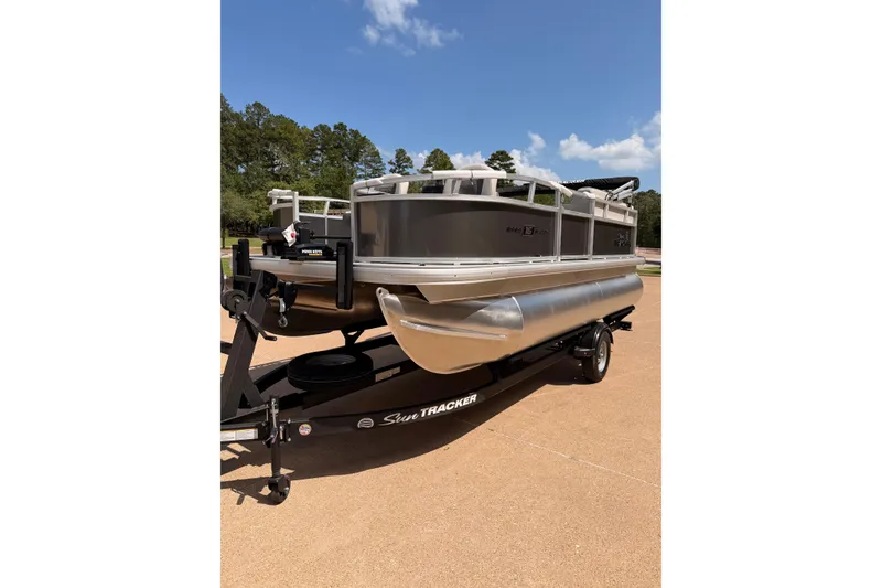 The Image of 2026 Sun Tracker Bass Buggy 16 XL Select pontoon boat on trailer, parked outdoors. - 0