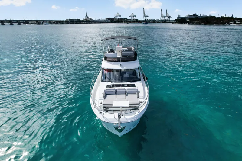 Slide: The Image of 2025 Jeanneau NC 1295 Fly yacht on clear turquoise water, with industrial backdrop. - 1