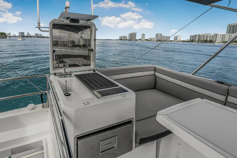 Slide: The Image of 2025 Jeanneau NC 1295 Fly yacht with outdoor kitchen and seating, overlooking a city skyline. - 13