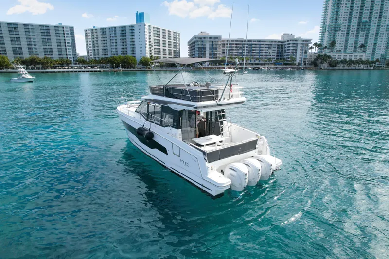 Slide: The Image of 2025 Jeanneau NC 1295 Fly yacht on clear blue water near urban skyline. - 2