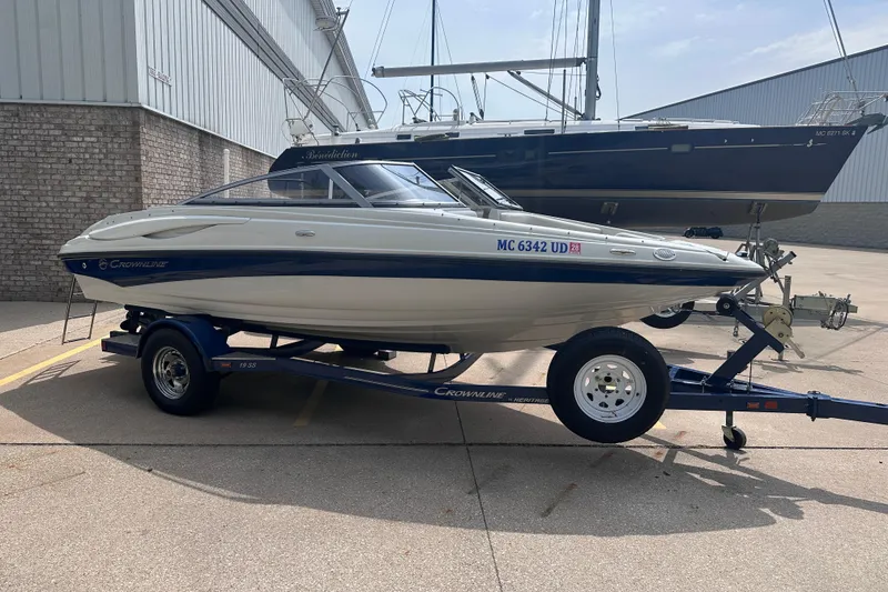 Slide: The Image of 2015 Crownline 21 SS boat on trailer, parked outdoors near a larger vessel. - 1