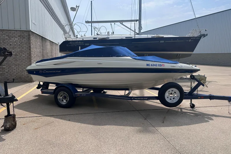 Slide: The Image of 2015 Crownline 21 SS boat on trailer, parked outdoors near a building. - 2
