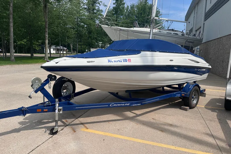 Slide: The Image of 2015 Crownline 21 SS boat on trailer, parked outdoors near trees and building. - 3