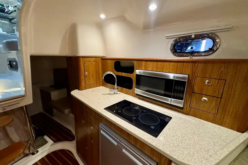 Slide: The Image of 2014 Pursuit OS 345 Offshore yacht interior with kitchenette, featuring stove, microwave, and wood cabinetry. - 18