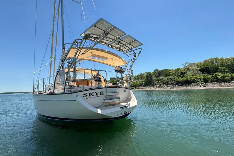 Slide: The Image of 2015 Island Packet 370 sailboat anchored near a lush shoreline under a clear blue sky. - 2