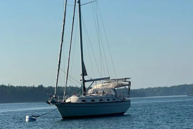 Slide: The Image of 2015 Island Packet 370 sailboat anchored on calm water with forested shoreline. - 8