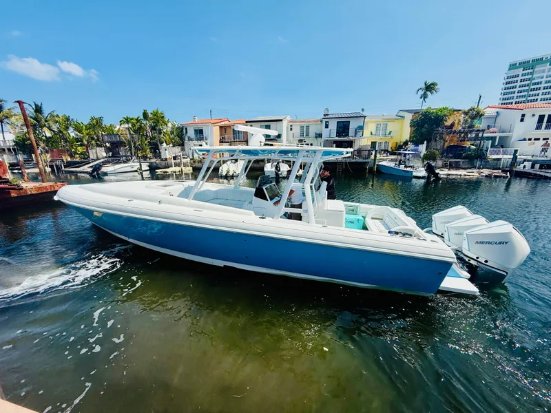 Slide: The Image of 2003 Intrepid 377 boat on water, blue and white, docked near waterfront homes. - 1