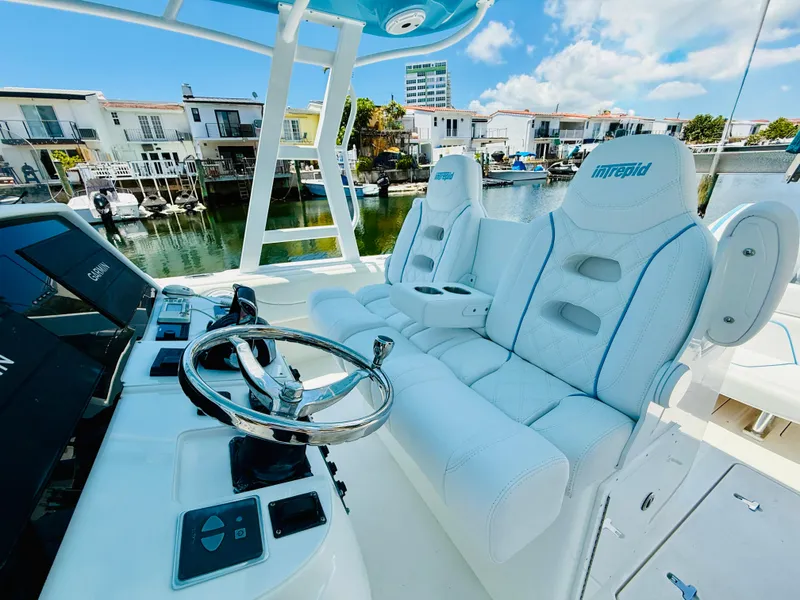 Slide: The Image of 2003 Intrepid 377 boat cockpit with white seating and steering wheel, docked near waterfront homes. - 26