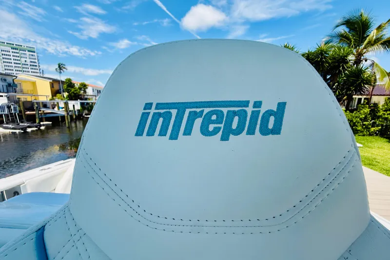 Slide: The Image of 2003 Intrepid 377 boat seat with logo, dockside view, clear sky background. - 54