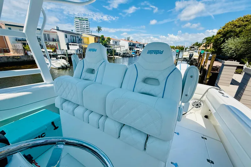 Slide: The Image of 2003 Intrepid 377 boat with luxurious seating, docked near waterfront homes under a clear blue sky. - 55