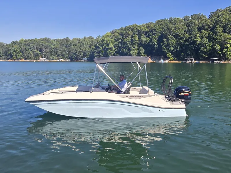 Slide: The Image of A 2027 Starcraft 181SVOB boat on a calm lake with a wooded shoreline in the background. - 22