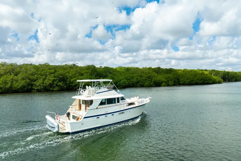 Slide: The Image of 1978 Hatteras 53 Yacht Fisherman cruising on a scenic river under a cloudy sky. - 12