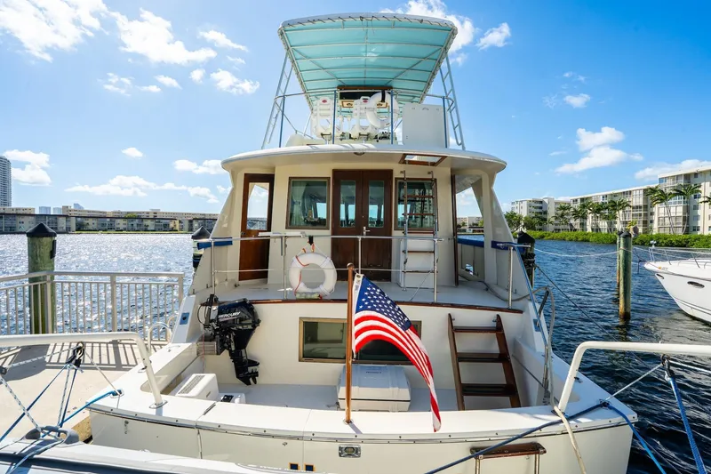 Slide: The Image of 1978 Hatteras 53 Yacht Fisherman docked, featuring American flag and sunny waterfront view. - 38