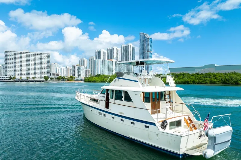 Slide: The Image of 1978 Hatteras 53 Yacht Fisherman cruising near city skyline and lush greenery. - 4