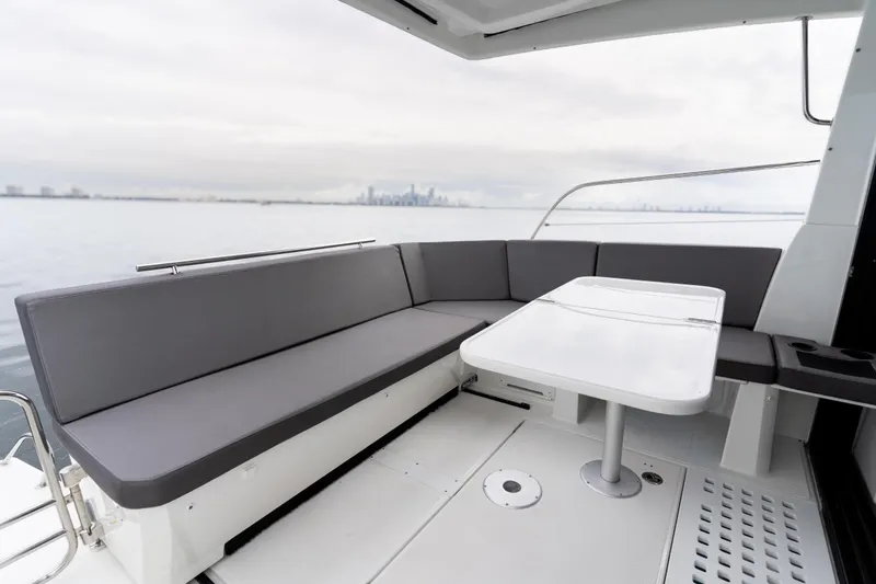 Slide: The Image of 2023 Beneteau Antares 11 boat deck with gray seating and white table, city skyline view. - 35