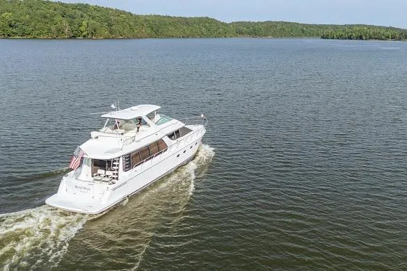 Slide: The Image of 2003 Carver 570 Voyager Pilothouse cruising on a serene lake with lush green shoreline. - 10