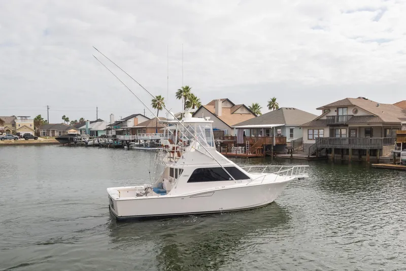 The Image of 2005 Cabo 35 Flybridge yacht cruising near waterfront homes under cloudy skies. - 0