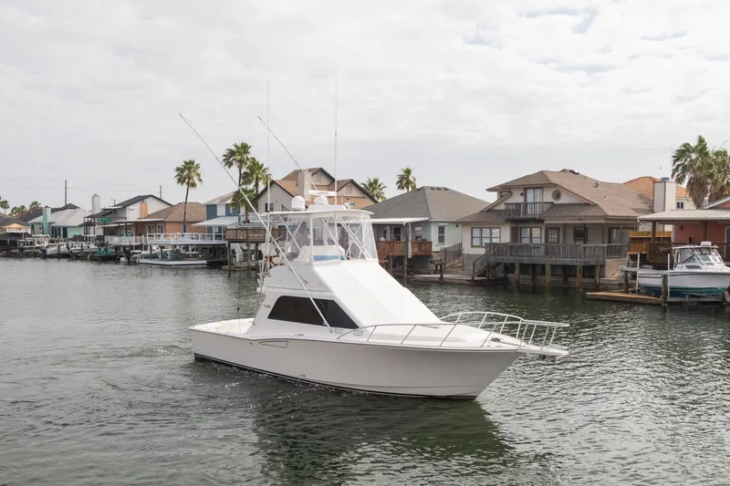 Slide: The Image of 2005 Cabo 35 Flybridge boat cruising near waterfront homes with palm trees. - 1