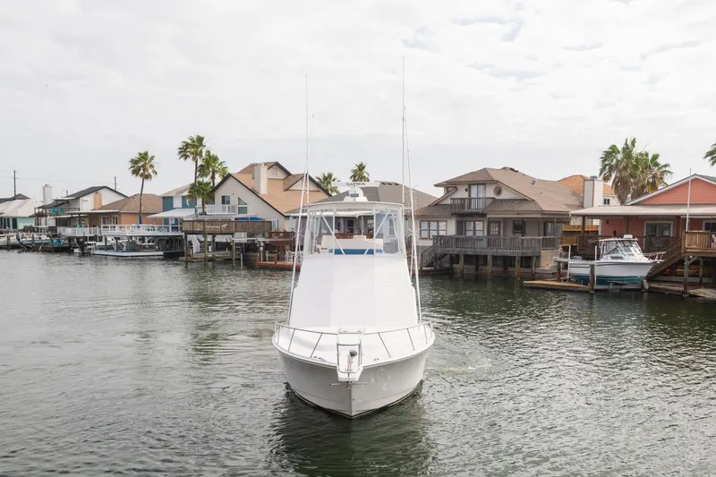 Slide: The Image of 2005 Cabo 35 Flybridge boat navigating a residential waterfront area with palm trees. - 2