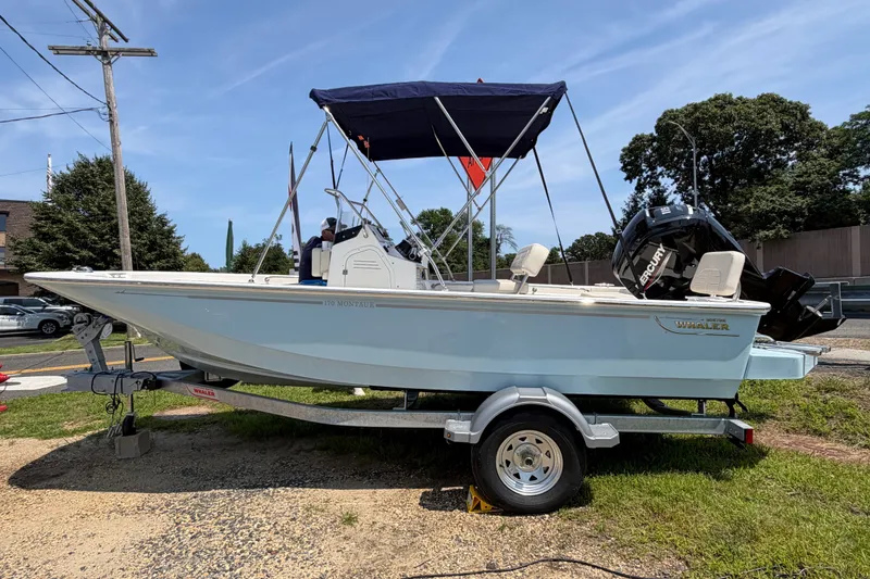 The Image of A 2027 Boston Whaler 170 Montauk on a trailer. It features a blue canopy and an outboard motor. - 0